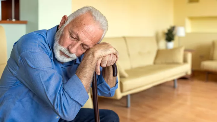 Older man sitting down leaning his head on his cane