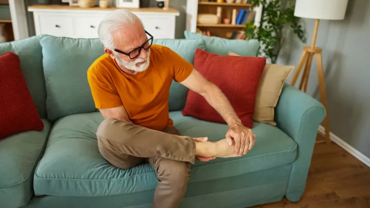 Man sitting on couch, holding foot in pain