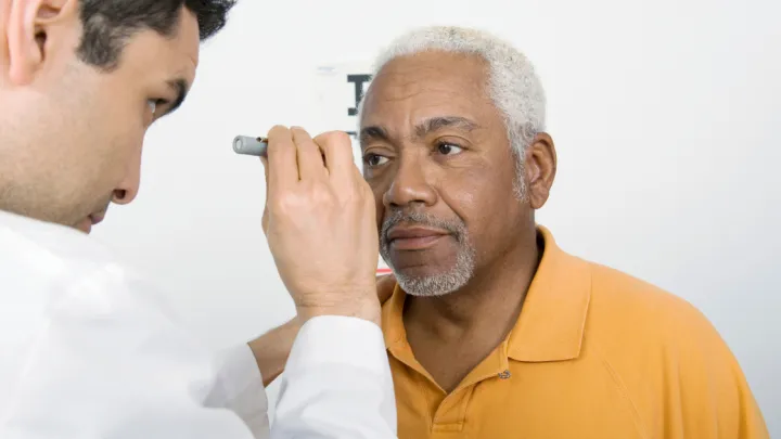 Eye doctor shining light in older man's eyes