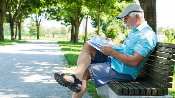 Man wearing compression socks, sitting on park bench reading