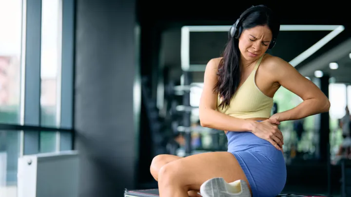 Woman in gym, sitting and holding hip in pain