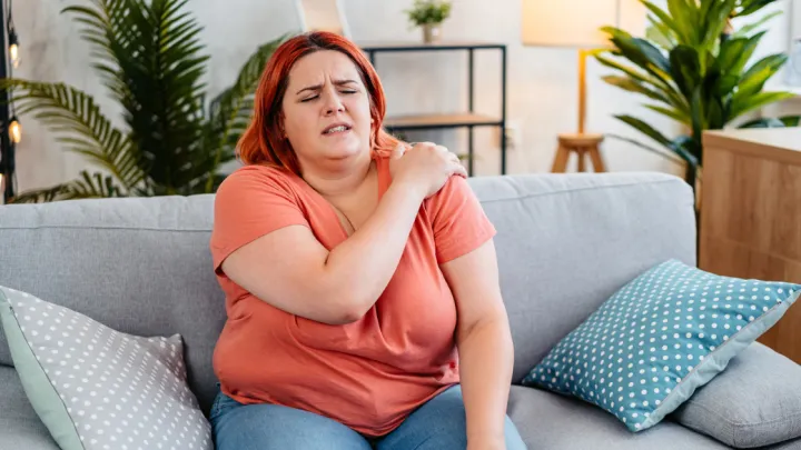 Woman sitting on couch holding her shoulder in pain