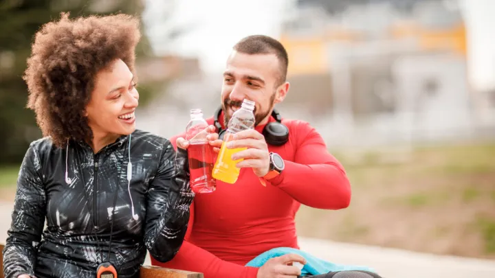 Man and woman sitting on bench drinking sports drinks