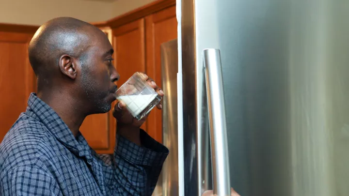 Man drinking a glass of milk in front of an open fridge