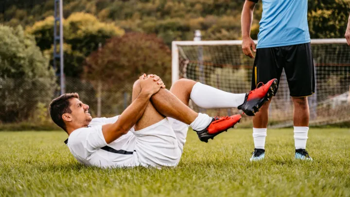 Soccer player holding his knee lying down on field