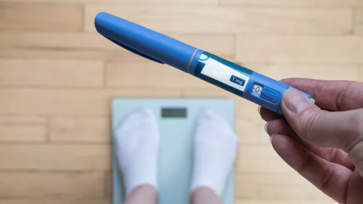 Close up of person standing on scale, holding GLP-1 injectable