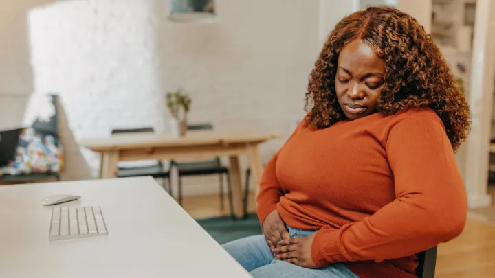 Woman sitting at desk holding abdomen in pain