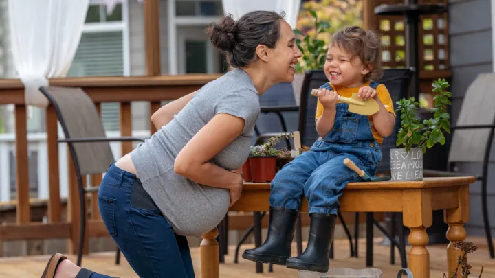 Pregnant woman laughing with her young daughter outside