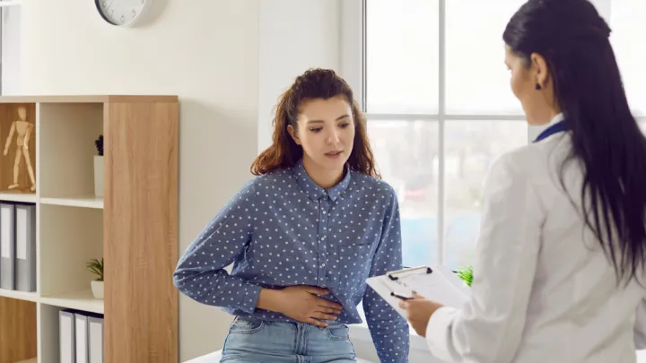 Woman holding abdomen talking to doctor