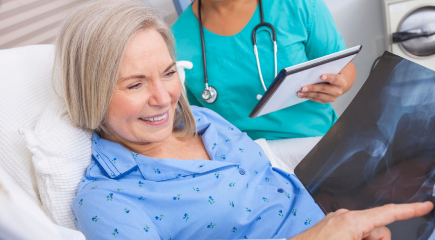 Woman in hospital bed looking at x-ray of hip