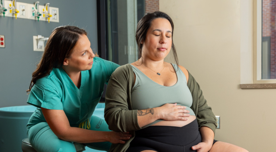 Pregnant woman sitting on exercise ball with midwife sitting behind her